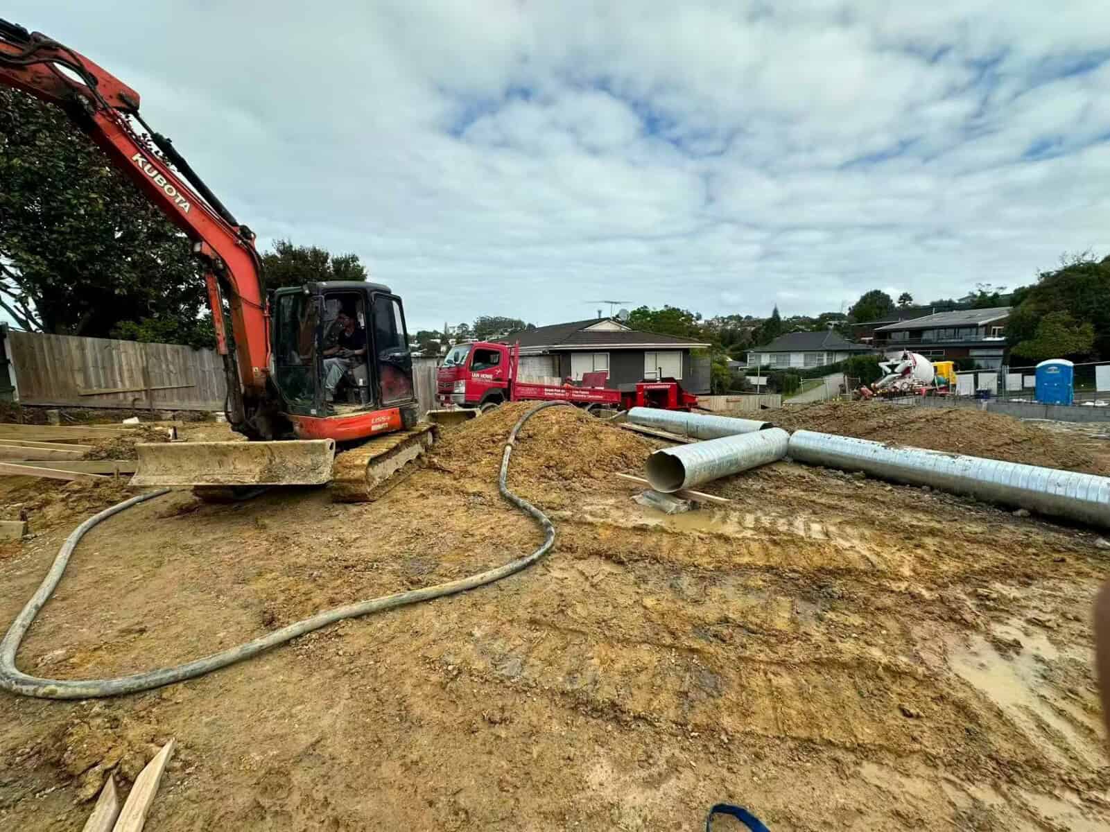 Excavator working on a cleared site with lengths of large-diameter stormwater pipe laid out ready to install