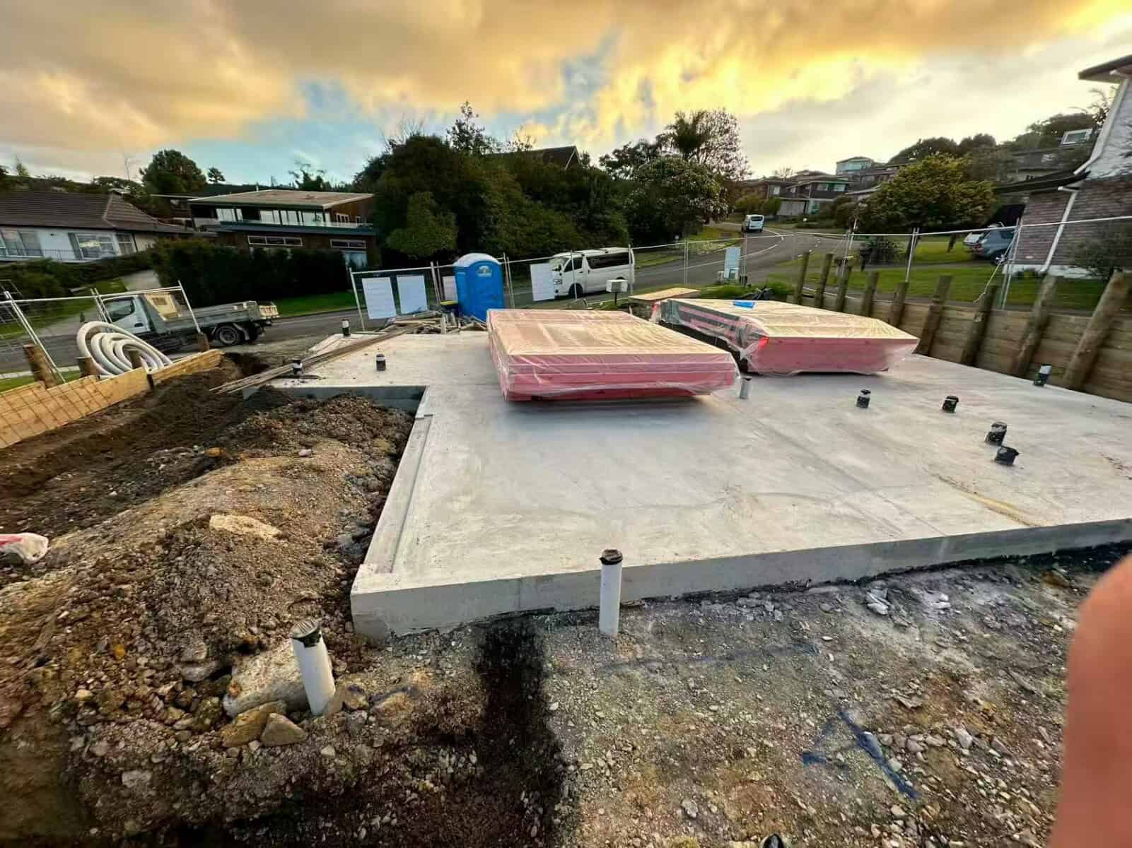 Poured concrete slab on a subdivision site at dusk, with formwork and building materials stacked beside it